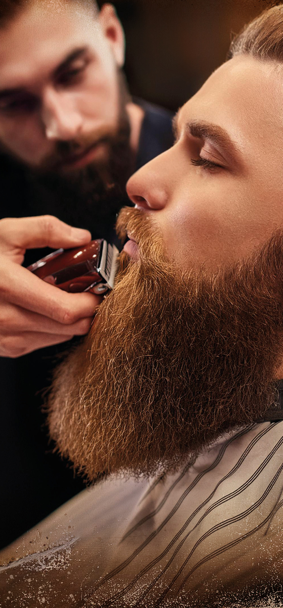 Un volto di un ragazzo, con la barba lunga bionda, presa di lato e una mano di un barberiere che gli sta tagliando la barba con la macchinetta rasoio
